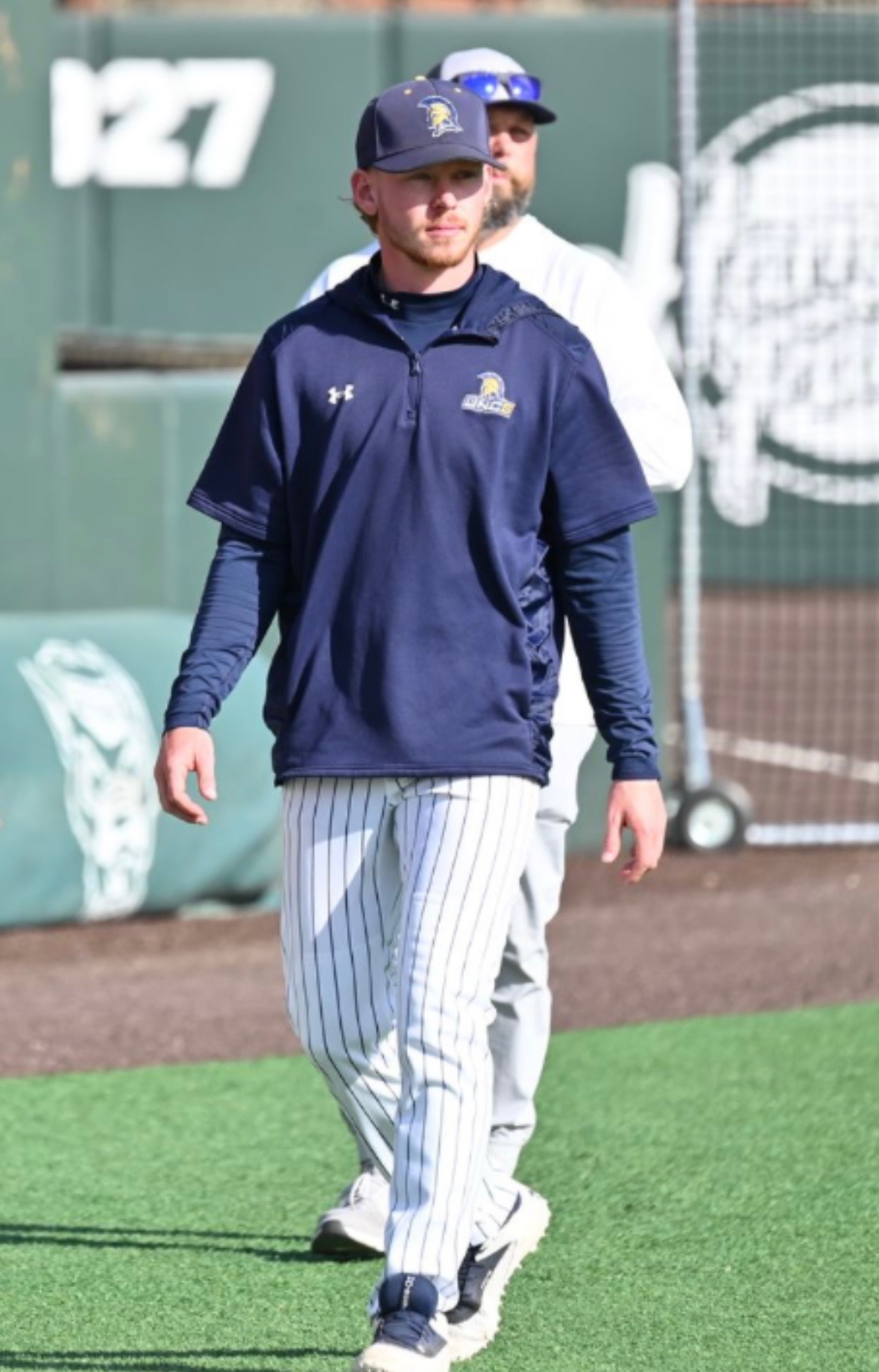 Tristan McAlister coaching on a baseball field in a navy pullover